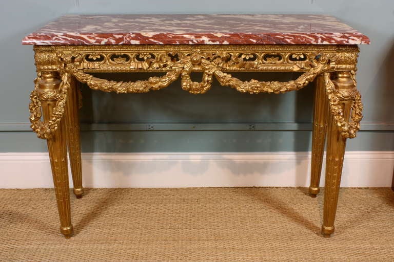 A stunning Louis XVI style gilded wood console table with nicely-carved neoclassical details, including a pierced apron, wreath and swags of rose garlands, tapered fluted legs, circa 1880. Console table has a beautiful red Languedoc variegated