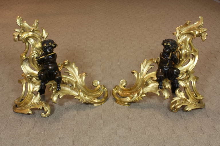 Large, high-quality pair of French gilded and patinated bronze chenets or andirons in the Louis XV style (Circa 1880), with fauns or hoofed wood nymphs, one playing a flute and the other holding a baton.  The chenets feature their original