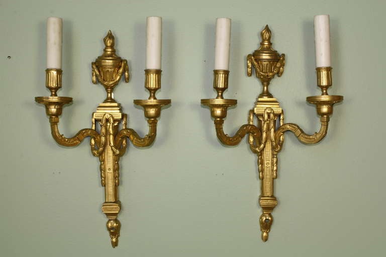 Pair of French gilt bronze Louis XVI neoclassical style sconces, circa 1880, with an urn and brazier finial decorating the top, swags draping the central portion of the sconces, acanthus leaf details on the arms and other neoclassical ornaments.