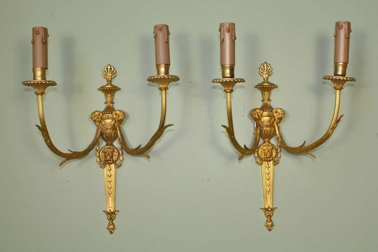 Zwei französische Wandleuchter aus vergoldeter Bronze im klassizistischen oder Louis-XVI-Stil, mit Widderköpfen am Fuß der Arme, zentraler Löwenmaske, Anthemion-Blatt-Finiale und Glockenblumen am unteren Ende des Körpers (um 1880).  Die Arme sind