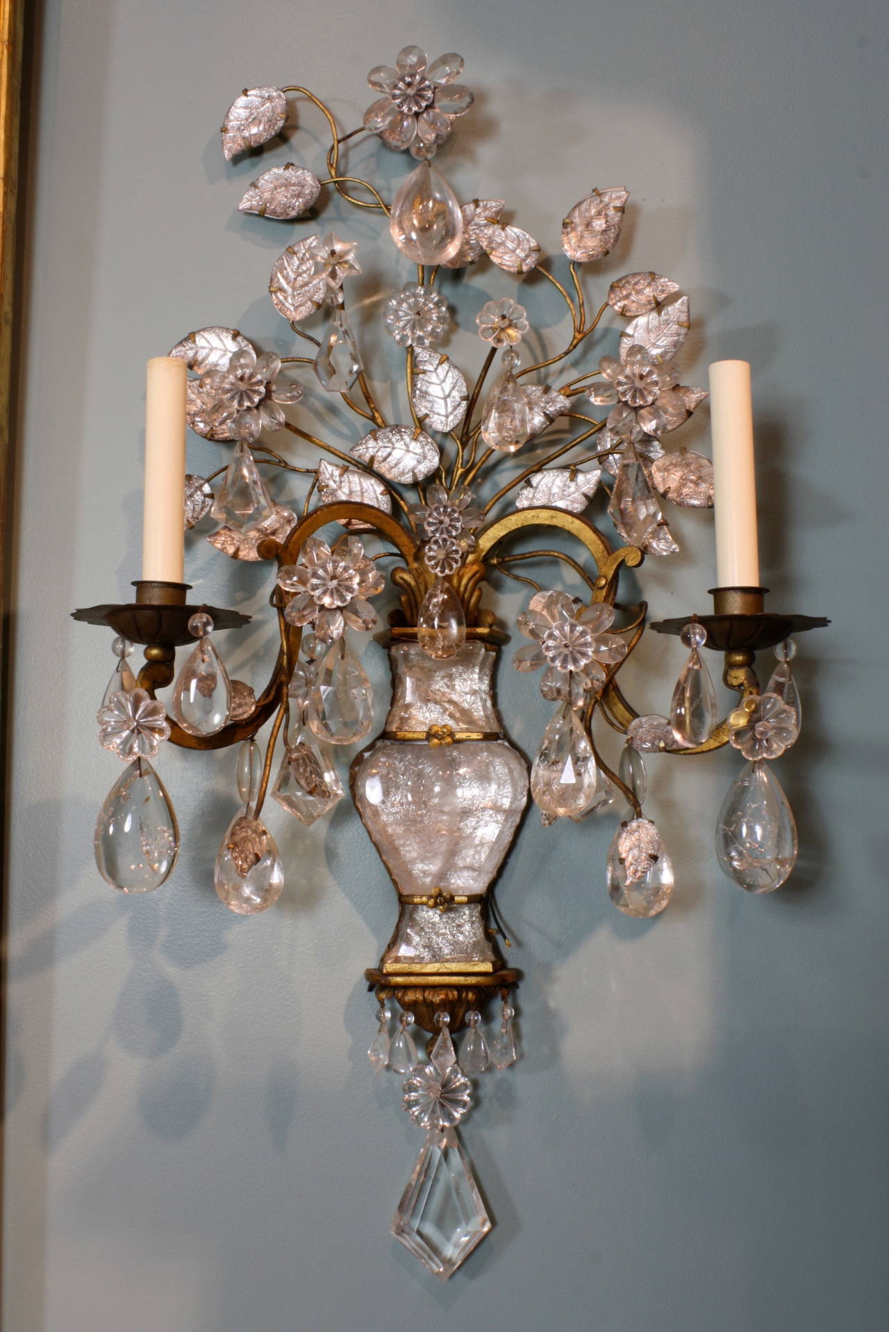 A large and highly-impressive pair of French gilt-metal, glass and rock crystal two-arm wall sconces, attributed to Maison Baguès (circa 1950), richly decorated with glass leaves, a variety of high-quality cut-crystals and rock crystals and flower
