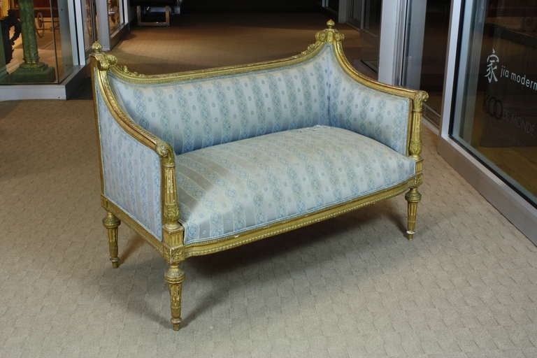 An elegant, petit French giltwood upholstered canape or settee in the Louis XVI style (Circa 1880).  Canape has nicely sloped back, terminating in finials with carved floral details, scrolling acanthus leaves on arm supports, stop fluted legs, water