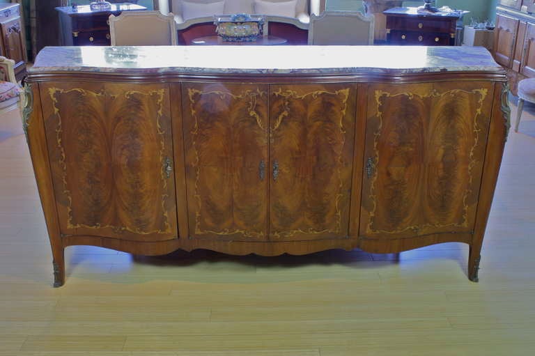 An impressive serpentine form mahogany buffet with highly-variegated breccia marble top, and nice vine and floral marquetry patterning around the doors and sides, bronze hardware, with three working locks and keys.  Buffet has four doors, with inner