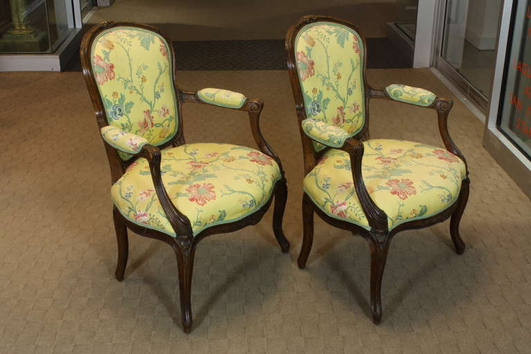 A pretty pair of French Louis XV period fauteuils, circa 1760, in carved fruitwood with floral lamps fabric. Cabriolet backs, nicely carved and molded arms, and delicately carved flowers decorating the crest rail, seat rail and knees highlight this