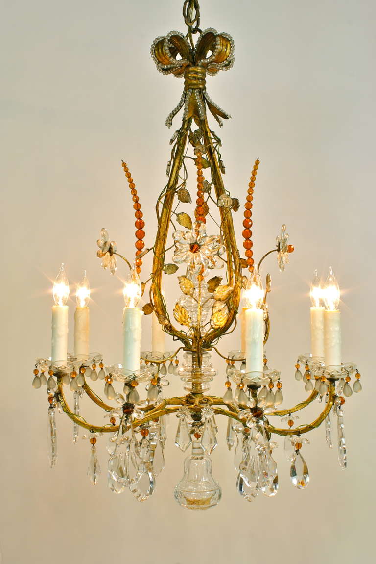 This incredible chandelier showcases the beauty and creativity of renowned French manufacturer Maison Baguès (Circa 1940-50s).  The frame is gilt-metal and is entwined with vines with leaves, and finer vines composed of small green glass beads.  The