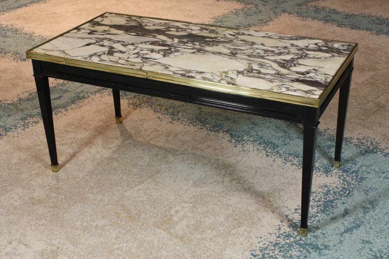 A sleek French black lacquered cocktail or low table with tapered legs, bronze mounts and rim, and nicely veined black, white and gold marble top (attributed to Maison Jansen, circa 1940).