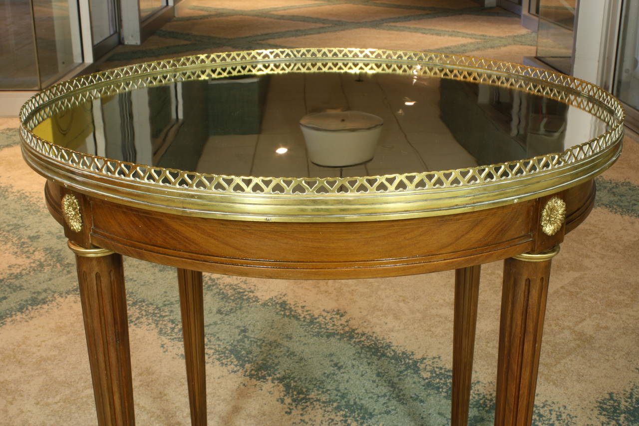 An elegant French gueridon in the Louis XVI style, with tapered fluted legs, gilt-bronze mounts and pierced bronze galley.  Table has its original mirrored glass top.