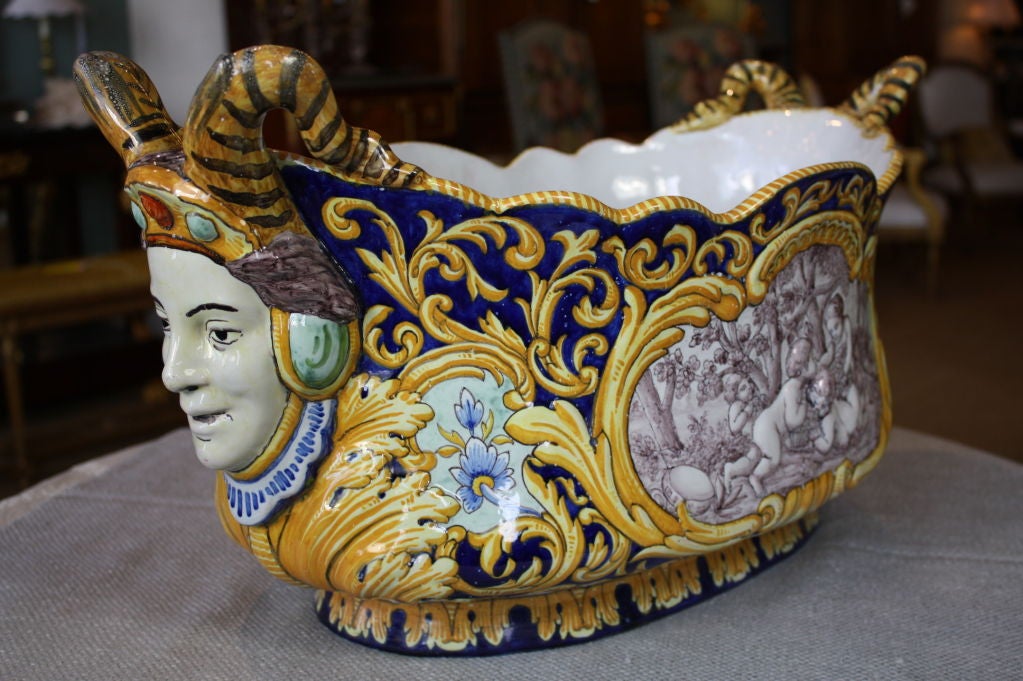Impressive, large hand painted French faience jardinière with jesters' heads as handles. Each side feature a different painted scene of putti playing in the woods inset into a background of cobalt blue and gold floral painted detailing. Marked