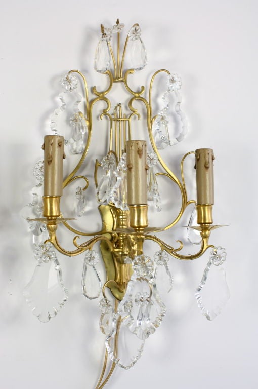 Pair of elegant french gilt-bronze and crystal sconces with three lights, in lyre form, with custom back-plates. Sconces have been regilded and have been re-electrified for the US.  Include new wax candle covers.