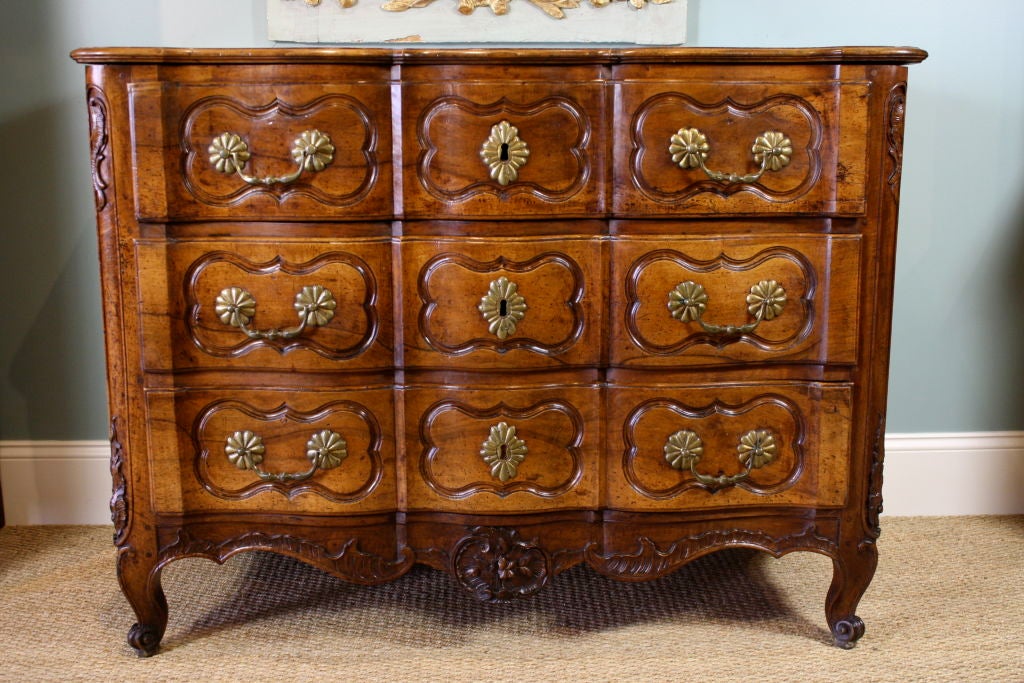 Beautifully carved French walnut commode (Louis XIV period, circa 1720) with three drawers in arbalete form, all four carved snail feet, nice foliate cartouche at the bottom, and original bronze hardware.