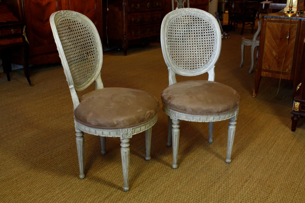 Pair of French Louis XVI style caned boudoir chairs.  Seats have taupe colored suede upholstery.  Very nice shell and floral carving on crest rail, floral motifs on joints, fluted legs and other neoclassical ornamentation.  Possibly 18th century.