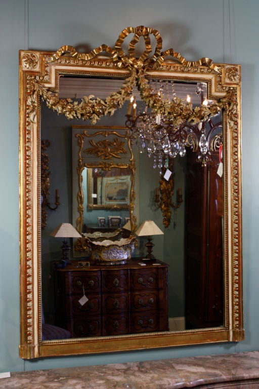 French Louis XVI style gilded and polychrome mirror with nicely-sculpted bow cartouche, floral garland swags, indented corners with rosettes, egg and dart molding and other neo-classical ornamentation, and with original glass.