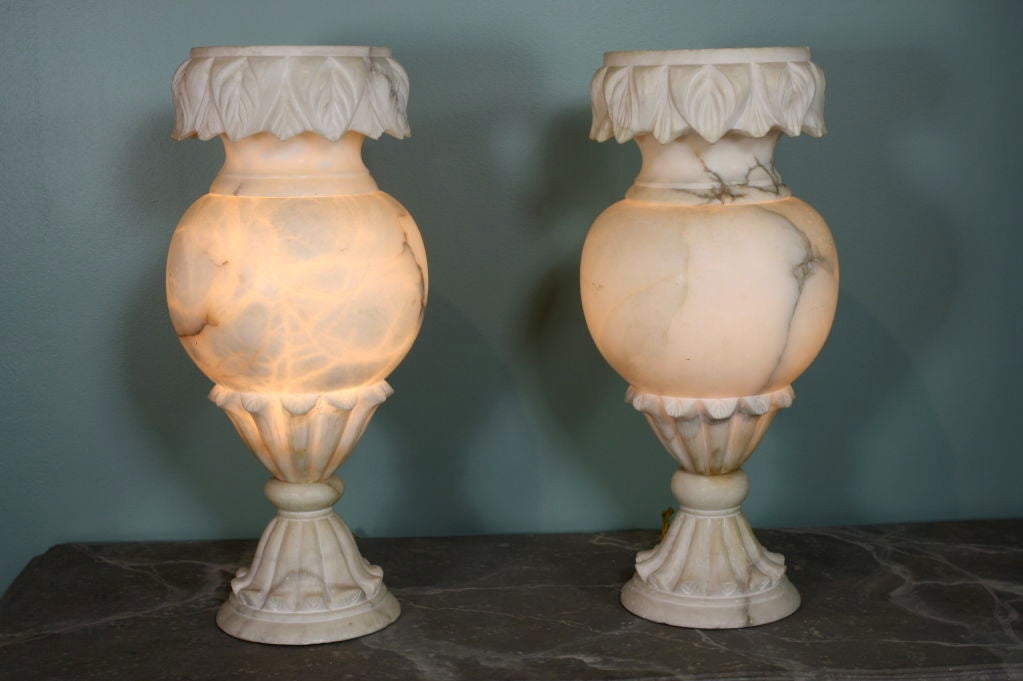 Pair of large, French carved alabaster vase-form lamps. Beautifully carved neoclassical details accent these vases, electrified as lamps and when lit are stunning in their appearance. The top part separates from the base.