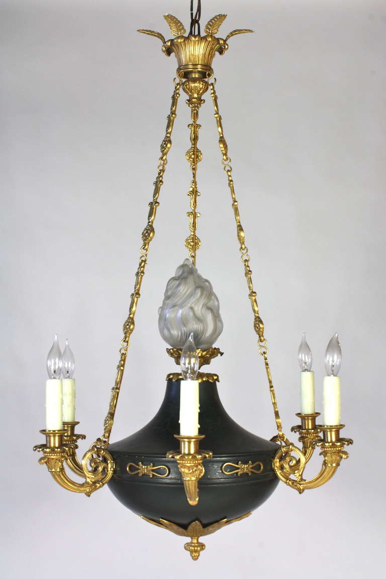 French Empire style chandelier with gilt bronze arms, neoclassical mounts, ornate chain and canopy. The central body is dark green painted wood, surmounted with a frosted glass flame finial. Wired for US with seven lights.