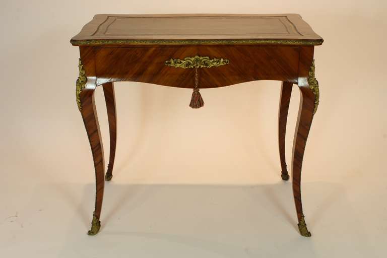 An elegant French Louis XV style petit writing desk with gilt-bronze mounts, including escutcheon, knees sabots and chutes.  One central locking drawer and a nicely embossed brown leather writing surface. Quality bois de rose marquetry.