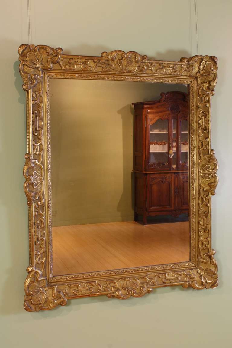 French Régence style carved giltwood and gesso mirror (late 19th century), with nicely-carved and molded stylized shells at the corners, detailed strap work, acanthus leaves, and other rococo forms.  Original glass and wooded back.