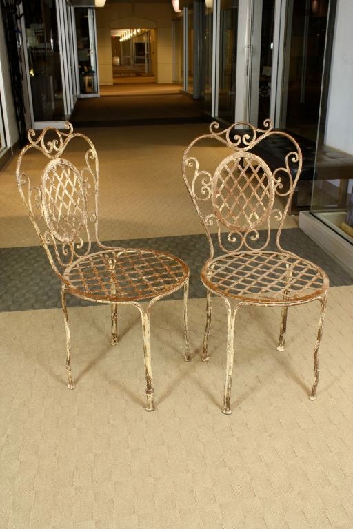 Pair of charming French painted wrought iron bistro chairs with lattice seats and backs. Frames decorated with 