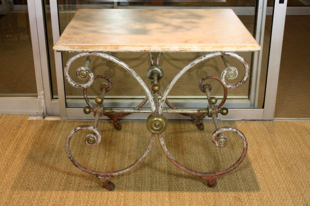 French iron baker's table with original marble top and bronze finials and other details.  The table is set on original bronze casters.  The scrolling frame has worn grey paint over the original red paint.  An excellent example of a true 19th century