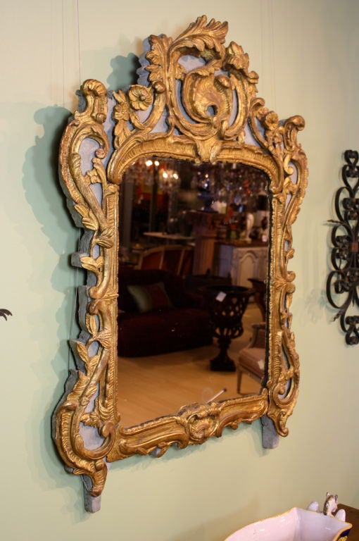 A nicely-carved and gilded Rococo trumeau mirror with greyish-blue painted background and old mercury glass, dating from the Louis XV period. The mirror is ornamented with deeply-carved rocaille elements, including a stylized shell cartouche,