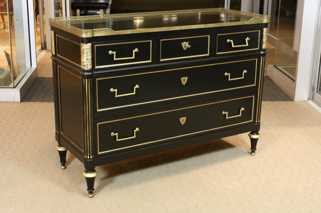An elegant French black-lacquered commode in the Directoire style by Maison Jansen.  The commode has a nice pierced brass gallery, bronze handles and lock plates, and gilded fluting, molding and other details.  It is fitted with three small drawers