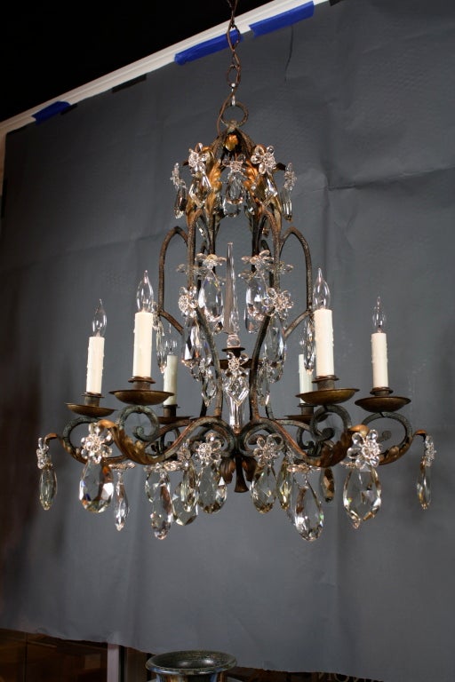 French iron, tole leaf and crystal chandelier with six arms, featuring many high-quality, large cut-crystal drops ornamented with crystal flowers, and a central cut-crystal spear over a crystal column.  In the style of Maison Bagues.