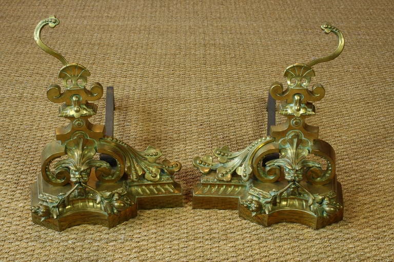 A pair of highly decorative French gilt-bronze andirons or chenets, with attached iron bars (circa 1870), in the form of fanciful dragons, with foliate berry, acanthus leaves and other naturalistic ornamentation typical of the Baroque style.