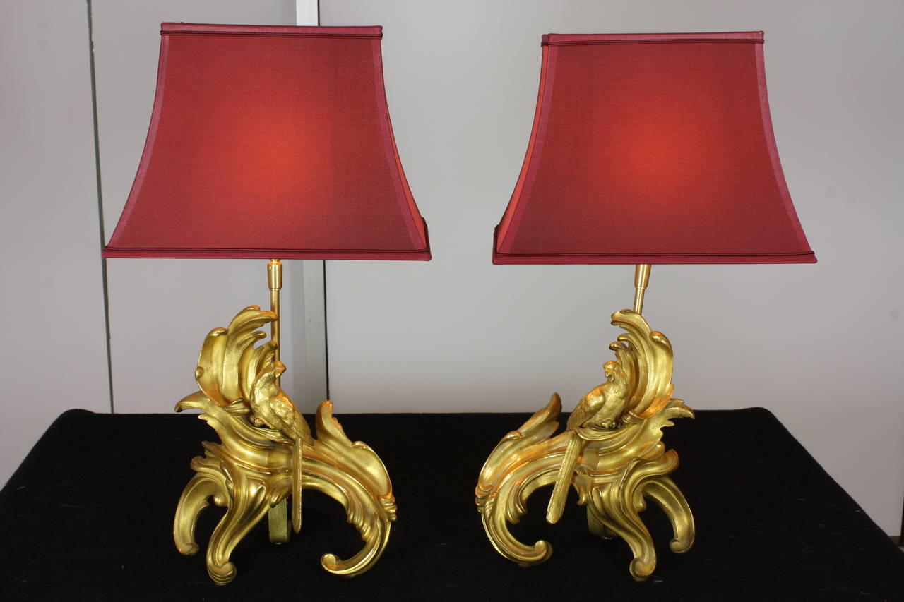 A high quality pair of French gilt-bronze Louis XV style chenets, with nicely-cast foliate detailing and featuring parrots (19th century), which have been converted to lamps (wired for U.S.), and include red silk over paper pagoda style shades.