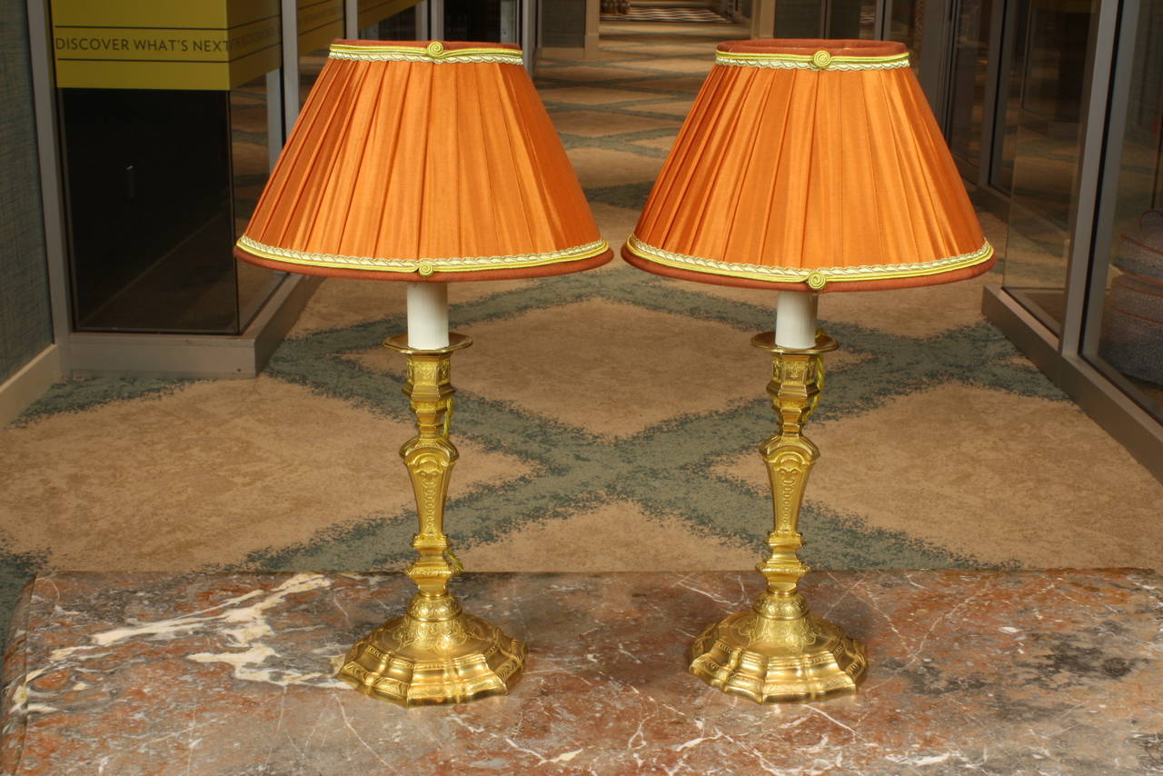 Pair of French Louis XIV style gilt bronze candlesticks, converted to table lamps, with recent French pleated silk lampshades. These lamps have been wired for the U.S.