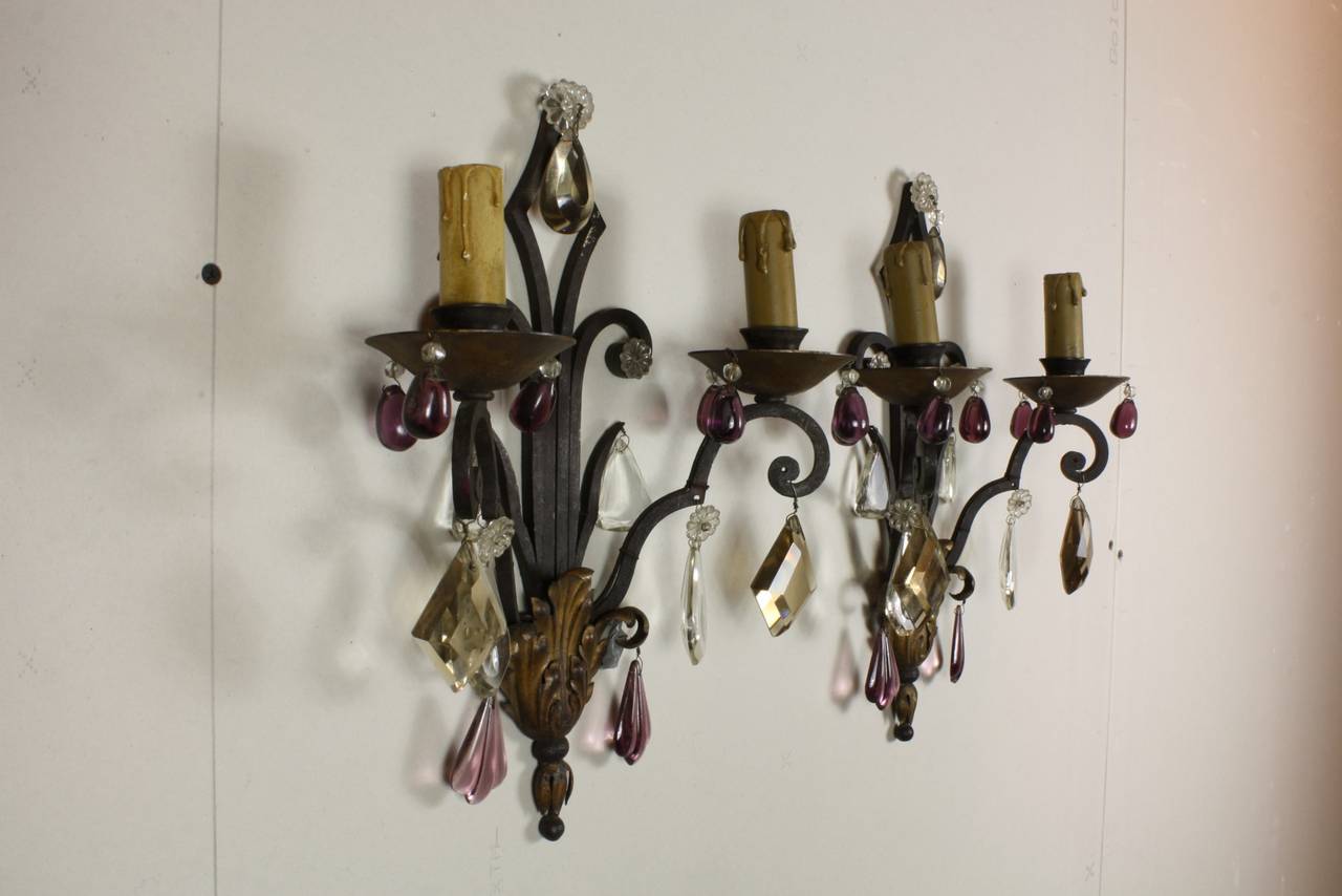 Pair of French wrought iron sconces with gilt-tole acanthus leaf detail and crystal drops.  The sconces are decorated with amethyst colored grape drops around the bobeches, smokey kite drops on the arms and amethyst-colored 
