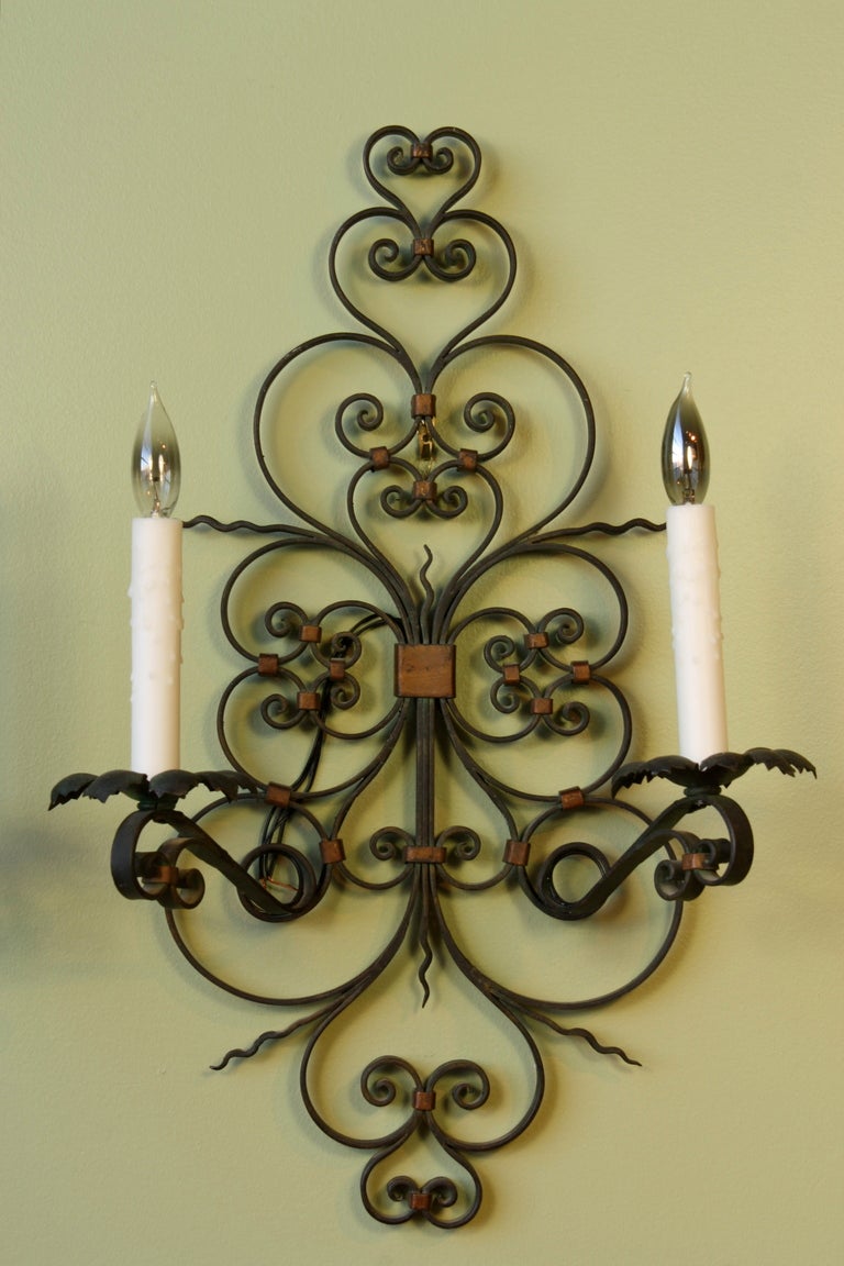 Pair of large French provincial wrought iron two-arm sconces with parcel-gilt and dark green paint. These sconces have been newly-rewired and have beeswax candle sleeves, and would make a charming addition to a French country or rustic interior.