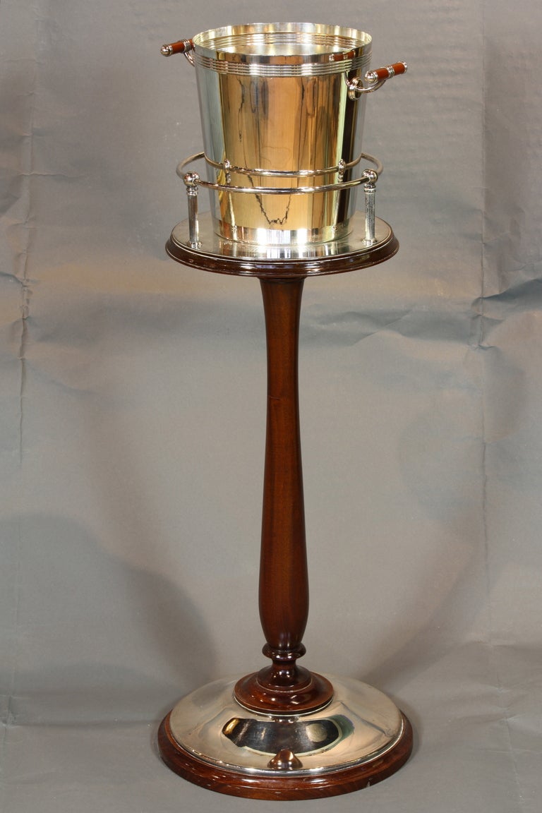 An Art Deco-inspired silver-plate wine bucket by Christofle on a silvered-plate and mahogany stand.  The bucket's handles are enameled.  It is very difficult to find a Christofle bucket with the stand. The stand alone stands 24-1/2