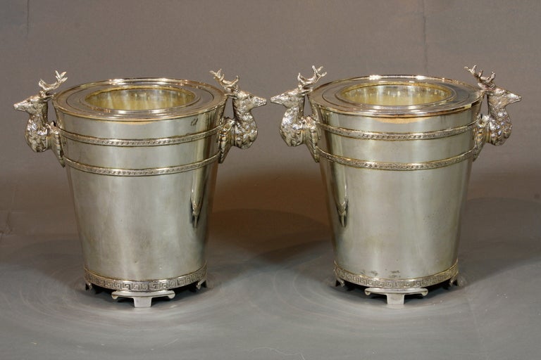 A pair of English silver-plated wine buckets with removable interior  inserts.  The wine buckets feature decorative stags' heads and Greek key design encircling the top and bottom of the buckets.  Each bucket is stamped underneath, 