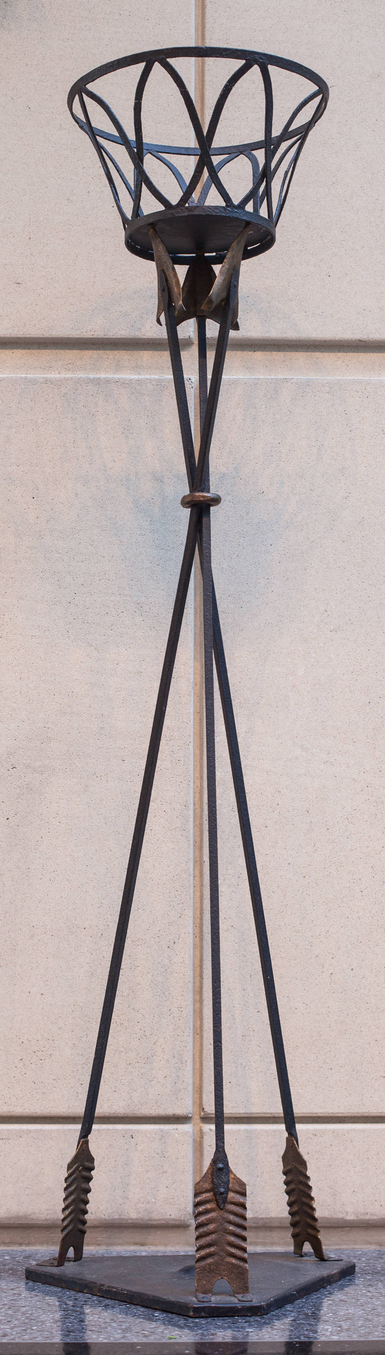 Neo-classical iron plant stand formed with three stylized long upright arrows.  The arrow heads and feathers are gilt.  The center iron ring holding the supports or arrows is also gilt.  The round latticed basket sits atop the arrows.  The weighted