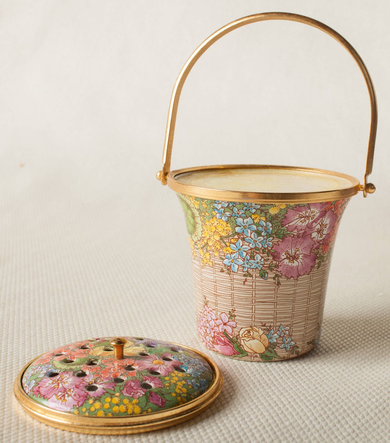 This is a very large piece of enamel work from Halcyon Days. It is in the form of a basket and functions as a potpourri holder. The delicate hand painted flowers are on a ground of wicker forming the basket motif. The handle, rim and knob are