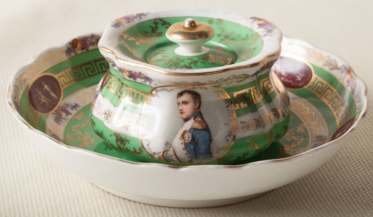 An image of Napoleon appears on this Austrian porcelain ink pot.  The hand painted portrait has the initials C.D. next to it.  The ground color is apple green with gilt Greek Key motif around the middle of the pot.  There are also colorful flowers