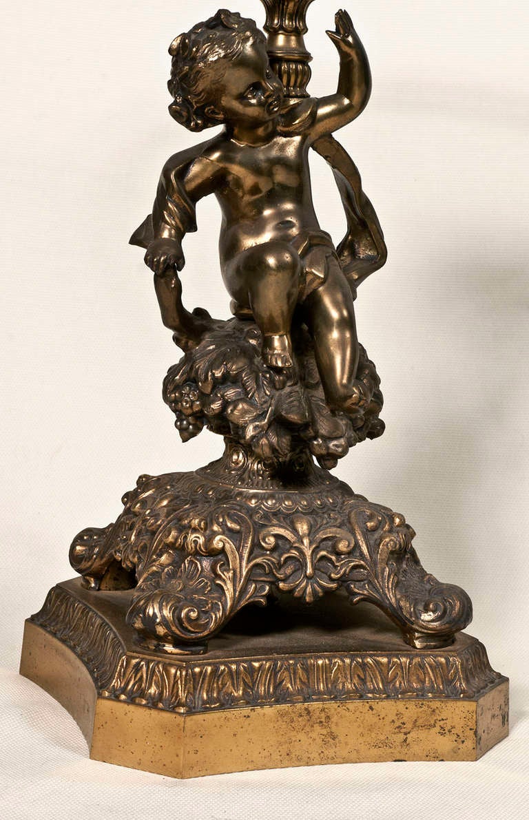 Pair of gilt brass and metal mirror image cherubs mounted on  brass cut corner bases.  The thick glass round tops have engraved and gilt star burst medallions on the underside.