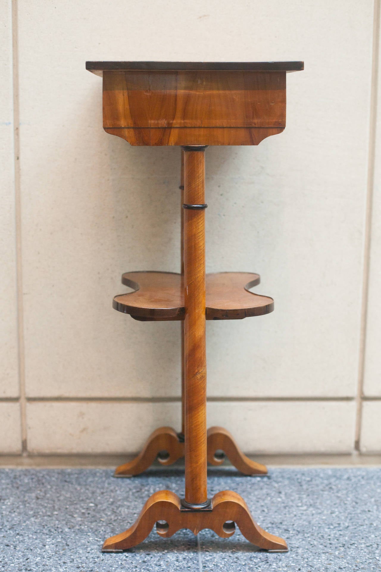 Austrian walnut Biedermeier sewing table with ebonized trim and one drawer below. The two columnar legs are supported by a shelf and a stretcher below terminating on downswept feet.