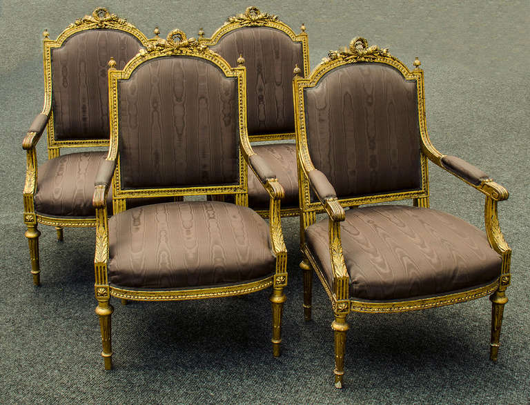 Set of four gilt hand carved wood Louis XVI style fauteuils.  The back top carving is of a laurel wreath tied up with ribbon and a crossed quiver of arrows with a torch surrounded by beautifully carved flowers. 

 You can also view the rest of the