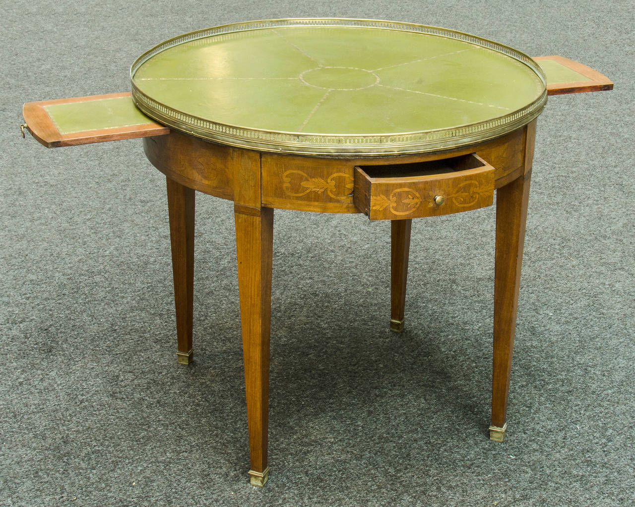 A bouillotte table was originally created for a card game of the same name. This one has a leather gilt tooled top with a pierced gallery. The apron has marquetry inlay. There are two drawers and two slides. Today these tables are great occasional
