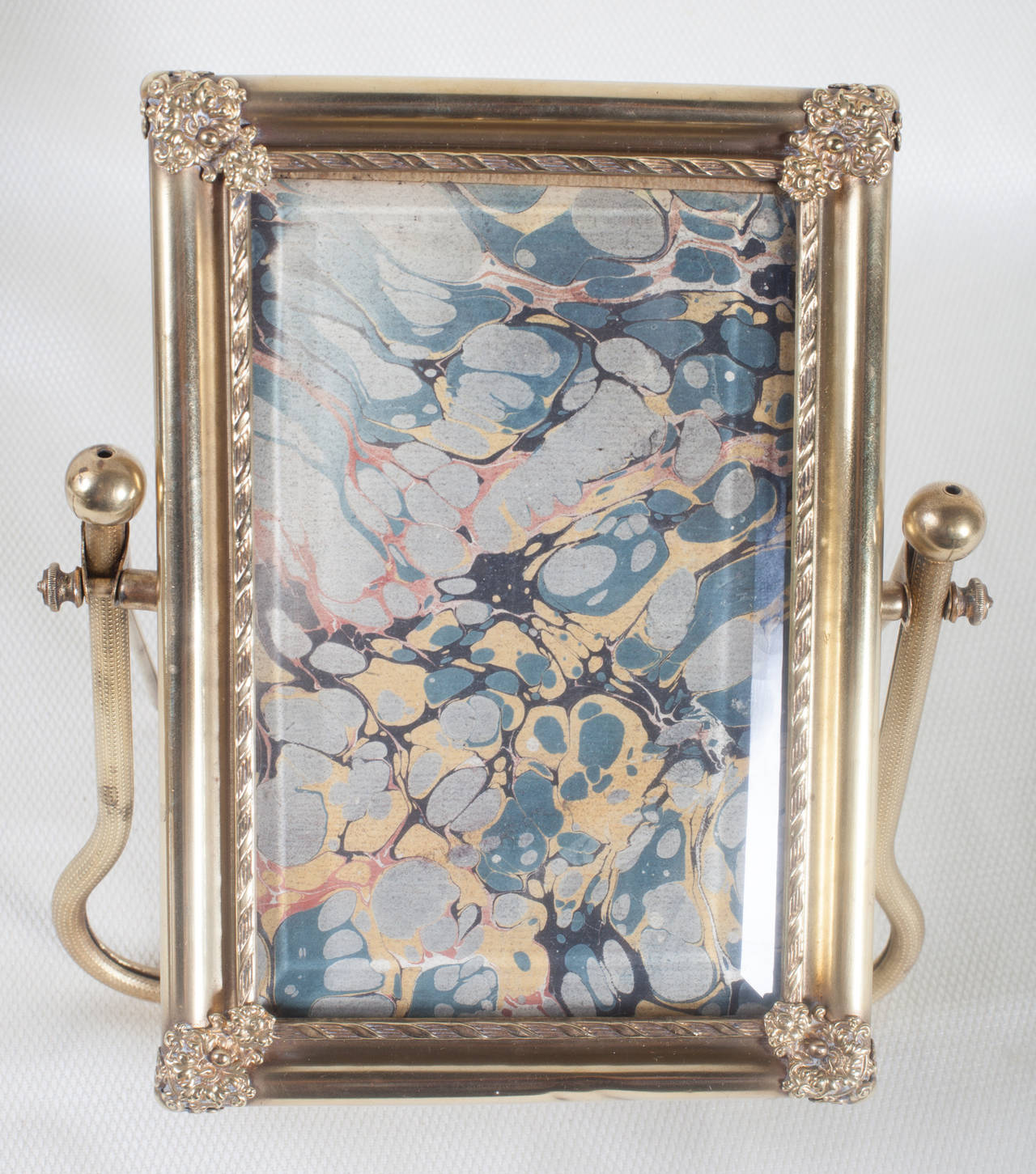 Antique French photo frame in the style of a cheval mirror. The gilt brass front support is engine turned. The rectangular frame has a fleurette in each corner and a twisted rope inner border. The thick glass is bevelled and backed with antique