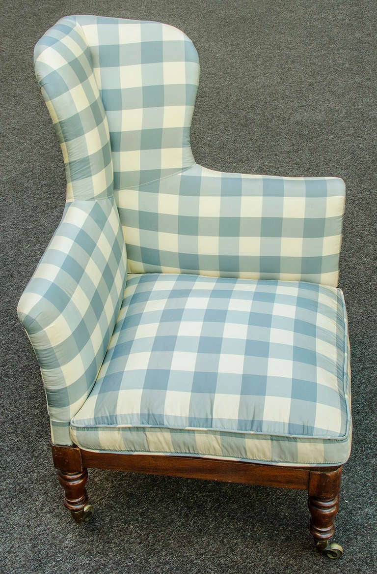 Rare mahogany corner chair with headrest.  Mahogany frame and caned seat with original brass castors on all four legs.  Upholstered in a blue and white silk check.  Makers stamp on underside of seat 