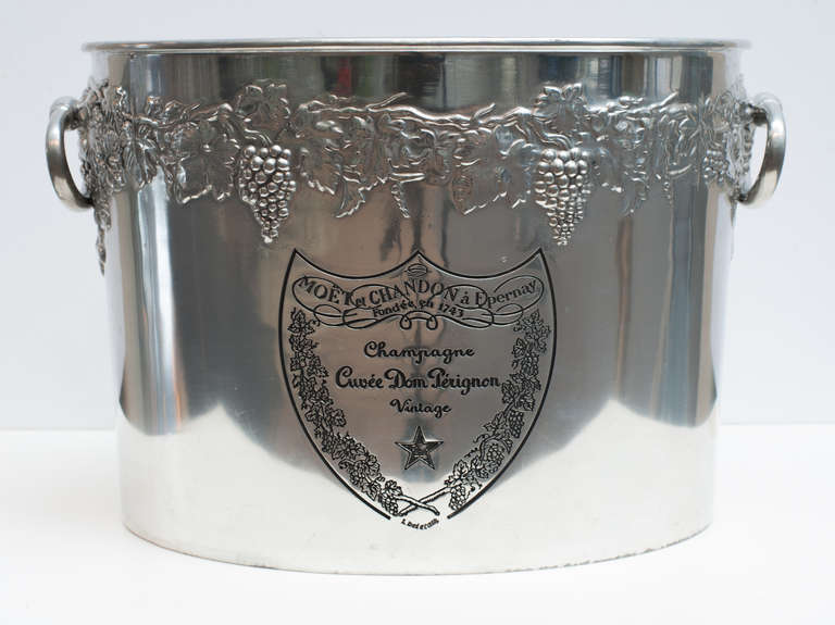 Solid pewter (8 lbs.) Dom Pérignon double champagne cooler.  The ovoid form has oval ring handles and a motif of grapes and grape leaves in relief around the top. The shield form of the company is both on the back and front.  These items were