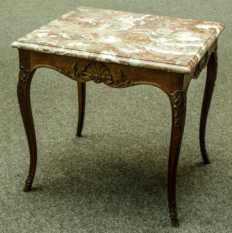 Louis XV center or occasional table in hand-carved oak with pegged construction and a marble top. Each of the four sides has a carved shell with an ancanthus leaf on each side. This motif repeats on the knees and again at the cloven hoof.