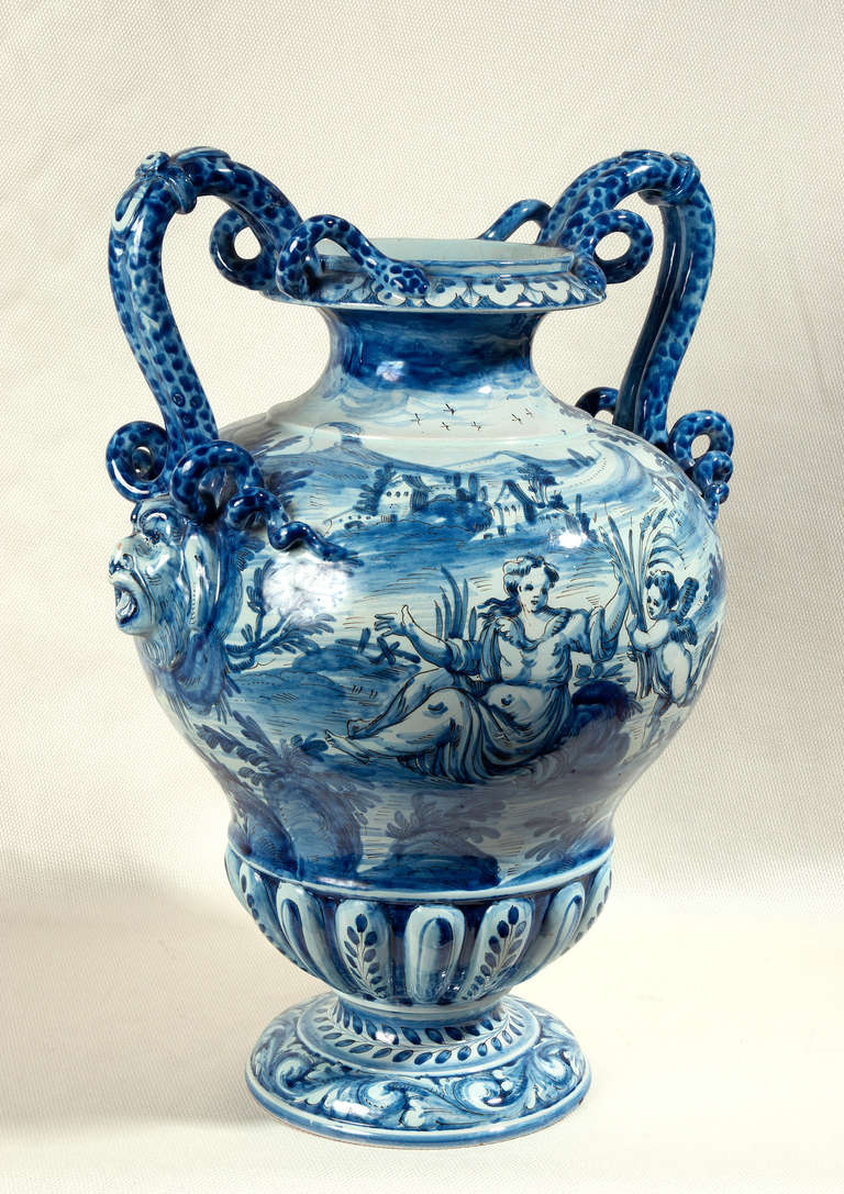 Cantagalli Italian majolica urn shaped vase.  The handles are double entwined serpents on top of a grotesque face.  The allegorical scenes anre hand painted in blue.  Marked on the underside is Cantagalli's trademark  of a hand sketched blue rooster.