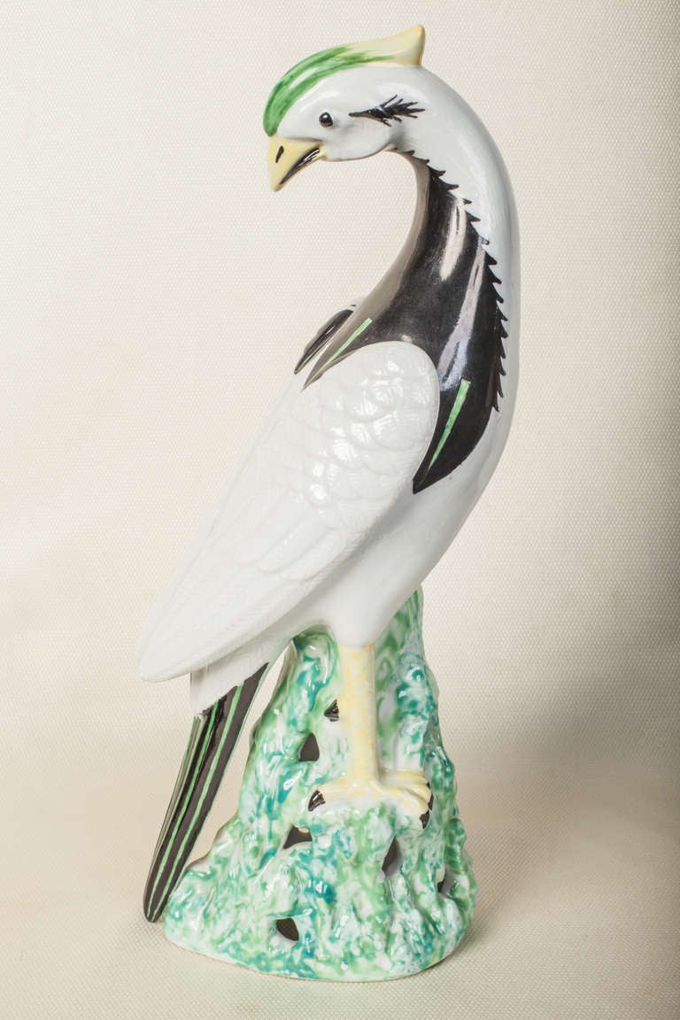 Tall exotic porcelain bird in the Chinese taste hand painted in black, yellow and green on a white ground.  The bird is standing on green rock work.  The detail on the back feathers is very fine.