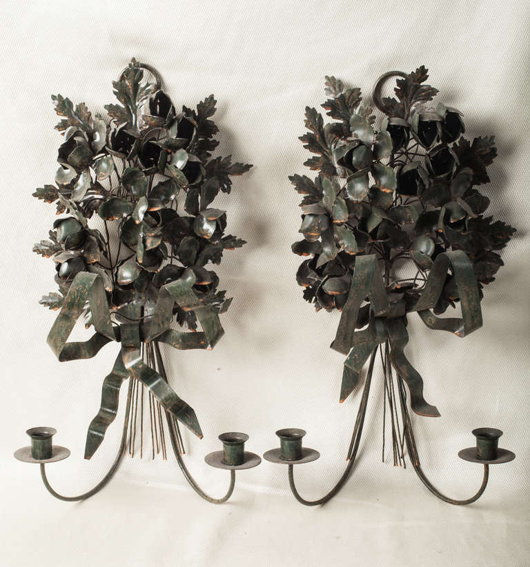 Pair of hand wrought tôle two light wall sconces.  Painted a very dark green these delicate bunches of flowers and leaves are tied up with a beautiful big bow.  They are in original condition and have not been electrified.