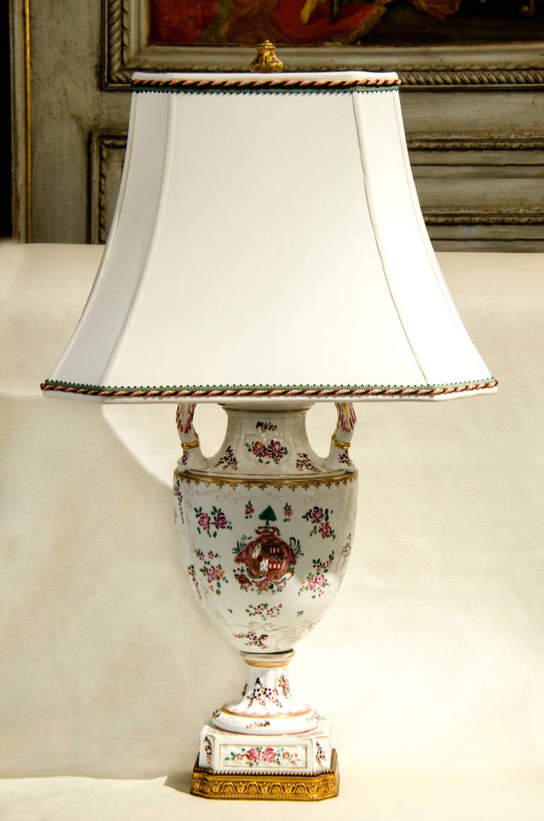 This antique hand painted armorial porcelain Samson two handled urn with cover has been custom mounted as a lamp. The porcelain is painted in lively pinks and purples with green leaves. There is a lot of raised white scroll work in the background