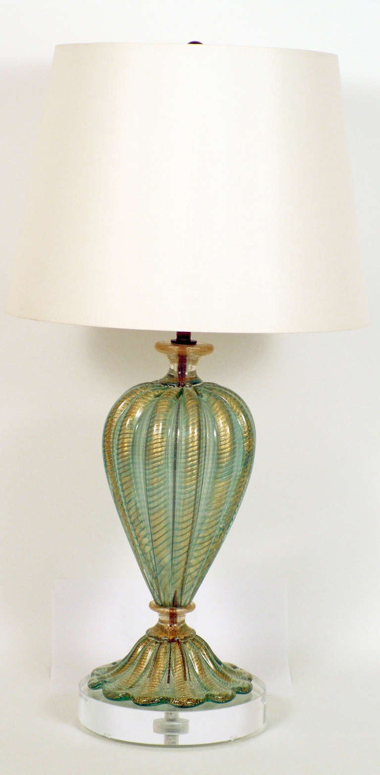 + Elegant Murano glass lamp that evokes glowing seafoam
+ Inverted teardrop tops wave-like base
+ Blue-green glass accented by metallic gold flecks
+ Deep ribs cover the entire surface
+ Newly added acrylic base