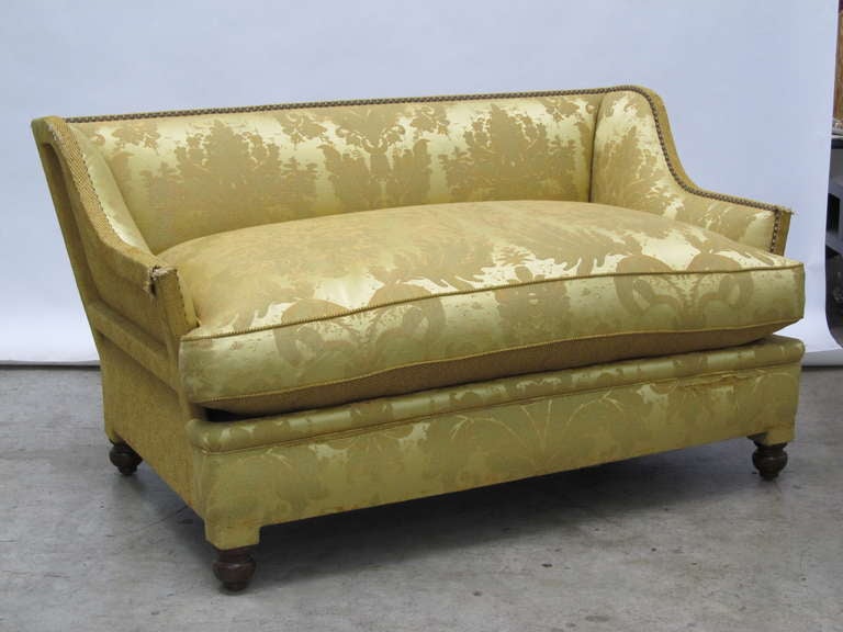 Loveseat covered in beige fabric and with wooden legs.