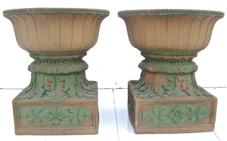 A rare pair of vintage, Early 20th Century, garden urns by the iconic Rookwood Pottery studio. Glazed, hard ceramic/terra cotta forms with high relief foliate and floral motifs. Beaded, petal-style bowl urns sit atop.Original garden-green finish.